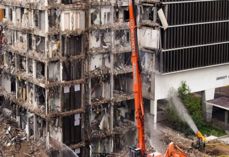 An orange excavator works alongside spraying water, conveying destruction and change in the USA.