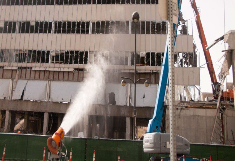 A dust suppression cannon sprays water on a building near a construction site in the USA