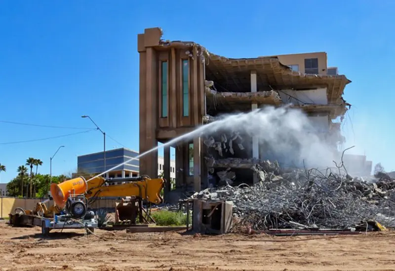 A water hose sprays to control dust, set against a clear blue sky in the USA.