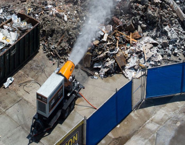 Machine spraying mist over a large pile of construction debris at a demolition site in the USA.