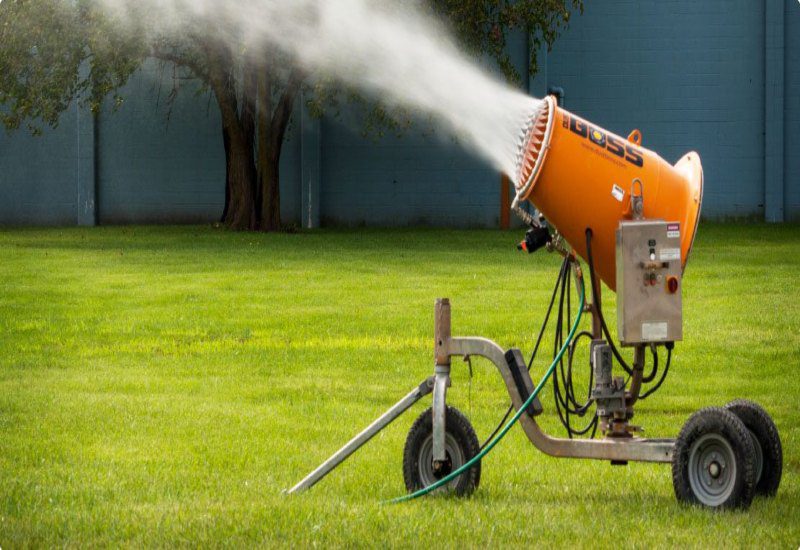 A sprayer releasing water over a grassy field for effective dust control in the USA.